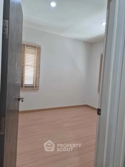 Spacious empty room with wooden flooring and natural light through windows.