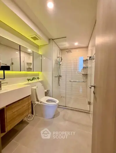 Modern bathroom with glass shower, sleek vanity, and ambient lighting.