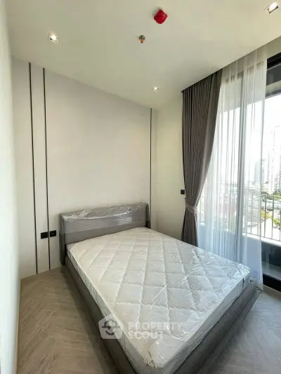 Modern bedroom with large window and city view, featuring a neatly made bed and elegant curtains.