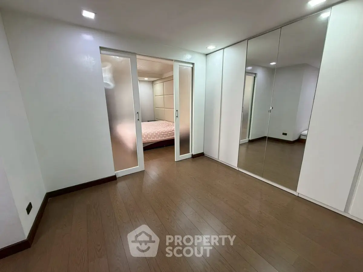 Spacious bedroom with mirrored closet doors and wooden flooring