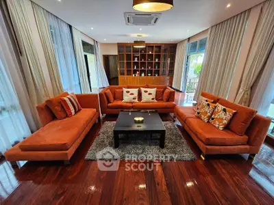 Luxurious living room with elegant orange sofas and large windows offering natural light and garden views.
