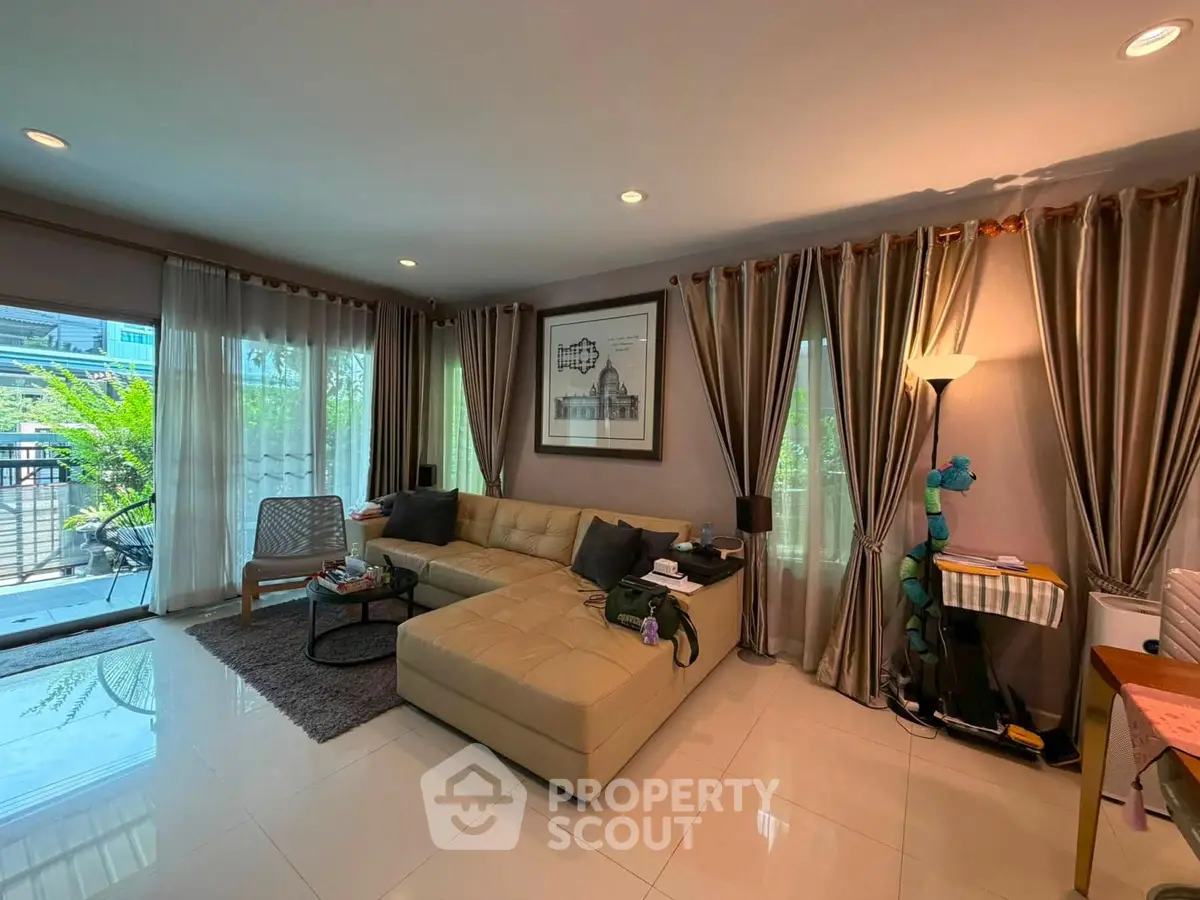 Spacious living room with modern decor and large windows opening to a balcony with greenery.