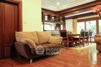 Spacious living room with cozy sofa and elegant dining area, featuring wooden flooring and large windows.