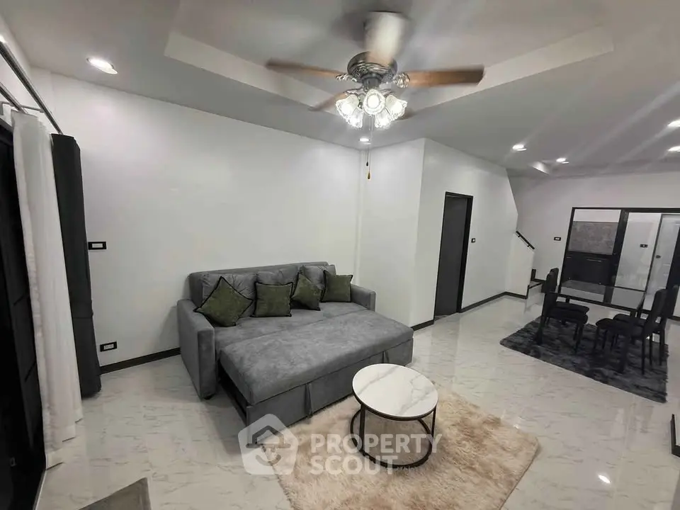 Modern living room with gray sectional sofa and ceiling fan, open layout to dining area.