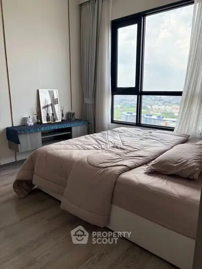 Modern bedroom with large window offering stunning city view, elegant decor, and cozy bedding.