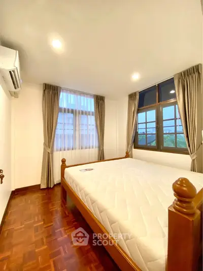 Spacious bedroom with large windows and wooden flooring in modern apartment