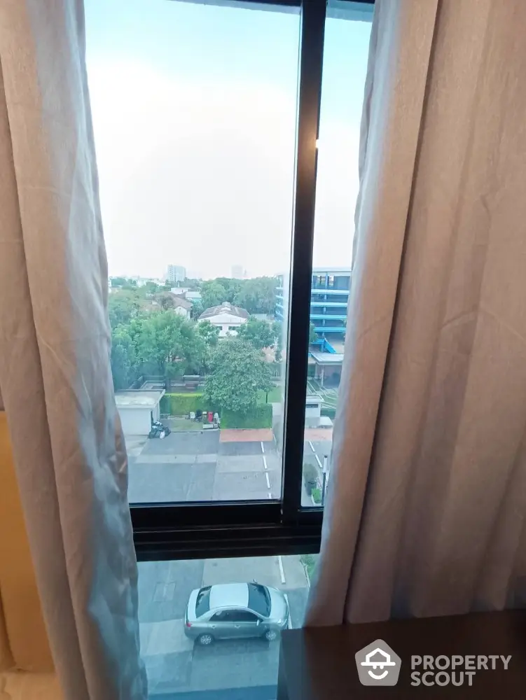 Bright window view from high-rise apartment overlooking cityscape and greenery.