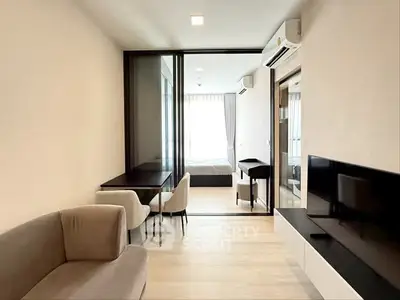 Modern living room with sleek furniture and glass partition leading to bedroom.