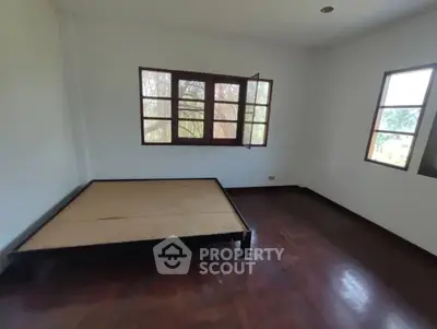 Spacious bedroom with wooden flooring and large windows offering natural light.