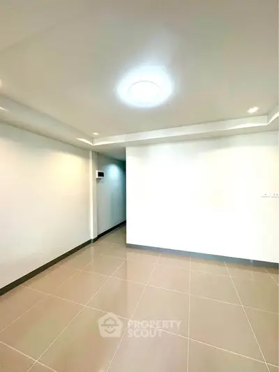 Spacious empty room with modern lighting and tiled flooring, perfect for customization.