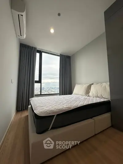 Modern bedroom with city view, featuring a comfortable bed and large window.