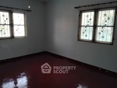 Spacious empty room with polished wooden floor and decorative window grills.