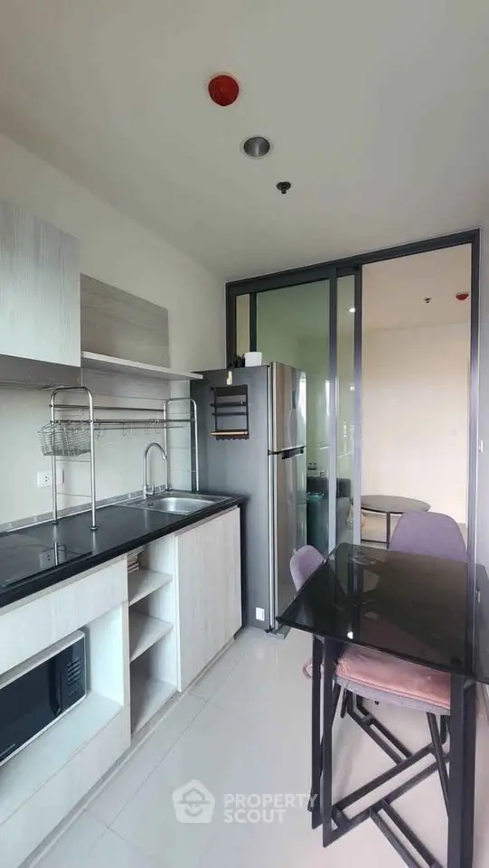 Modern kitchen with sleek design, featuring glass dining table and stainless steel appliances in a compact layout.