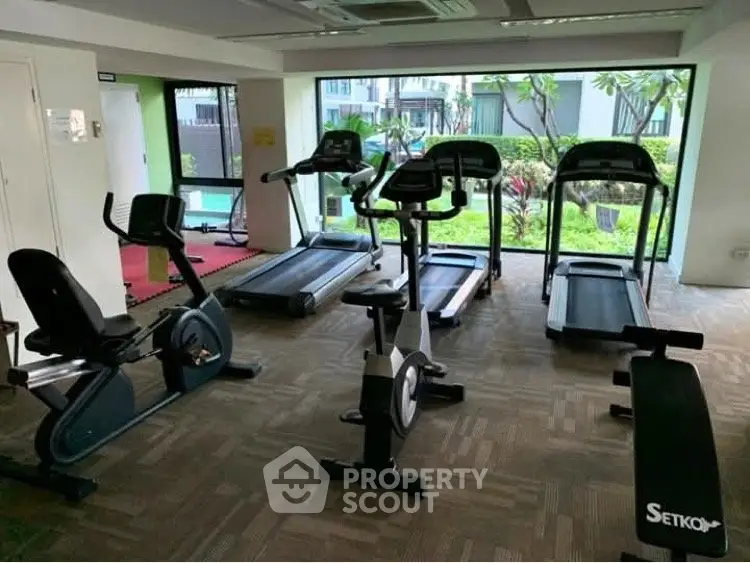 Modern gym with cardio equipment and garden view in upscale residential complex.