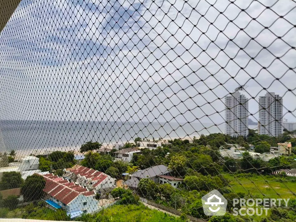 Stunning ocean view from high-rise balcony with safety netting, overlooking lush green landscape and modern buildings.