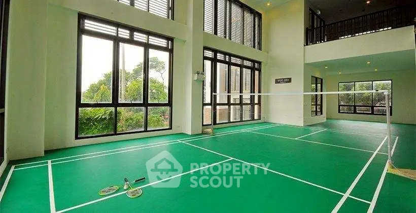 Spacious indoor badminton court with large windows and lush greenery view.