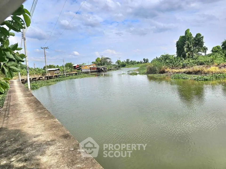 Scenic riverside view with lush greenery and distant houses, perfect for tranquil living.