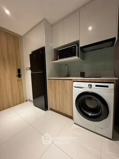 Modern kitchen with sleek appliances and wood accents, featuring a washing machine and fridge.