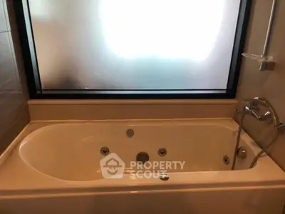 Luxurious bathroom with a modern bathtub and frosted glass window for privacy.