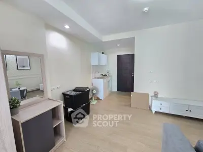 Modern living room with minimalist decor and compact kitchen area, featuring light wood flooring and neutral walls.