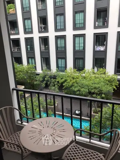 Charming balcony view overlooking lush greenery and a sparkling pool in a modern apartment complex.