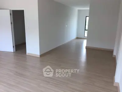 Spacious and well-lit empty living space with laminate flooring, ready for personalization, featuring large windows and a neutral color palette.