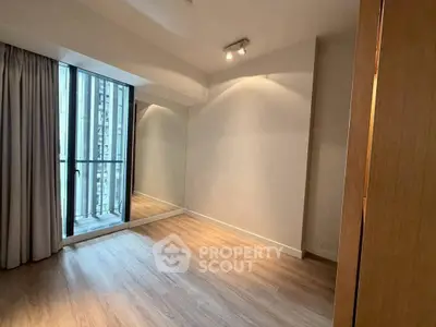 Spacious empty room with large window and wooden flooring in modern apartment.