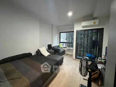 Spacious and well-lit studio apartment with modern furnishings, large windows leading to a cozy balcony, and sleek hardwood flooring.