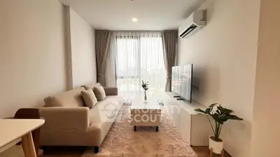 Modern living room with cozy beige sofa and large TV, featuring natural light and elegant decor.