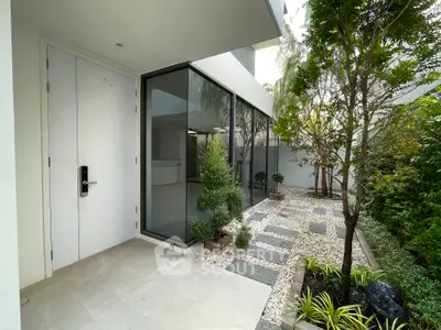 Modern home entrance with sleek glass design and lush garden pathway