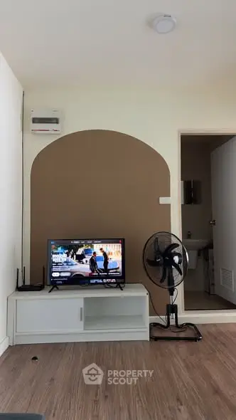 Modern living room with TV, fan, and wooden flooring in cozy apartment.