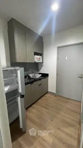 Modern kitchen with sleek cabinets, open fridge, and microwave in a compact layout.