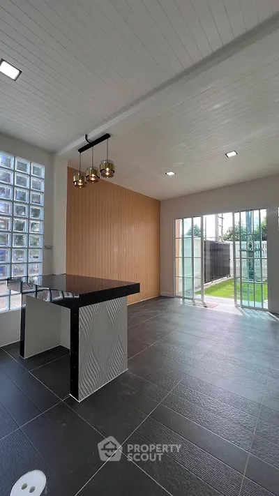 Modern open-plan living area with stylish lighting and large glass doors leading to a lush garden.