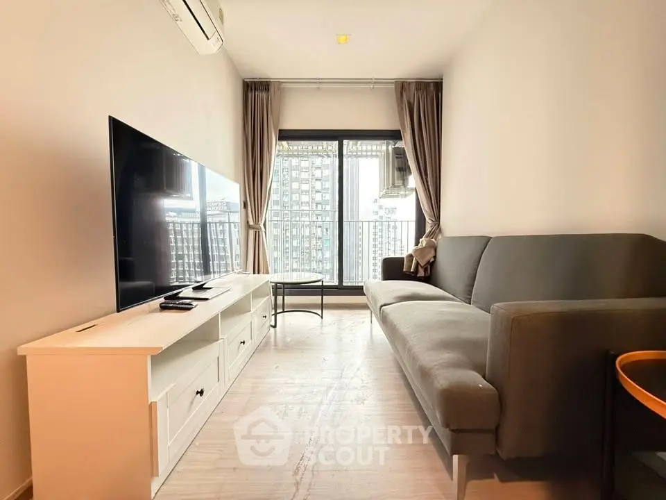 Modern living room with large TV and city view from balcony, featuring sleek furniture and natural light.