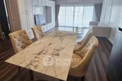 Elegant living room with marble dining table and plush chairs, featuring large windows and stylish decor.