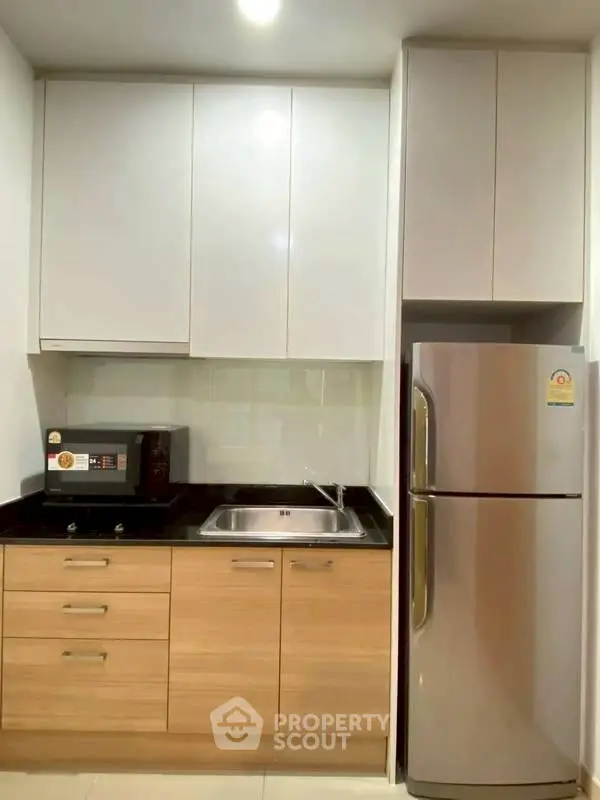 Modern kitchen with sleek cabinets, stainless steel fridge, and microwave oven.