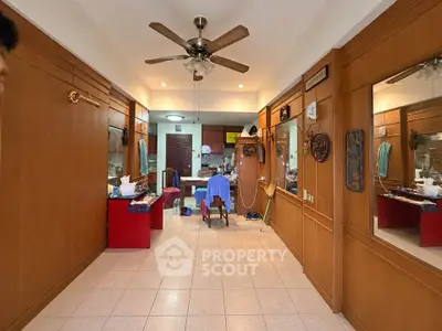 Spacious living room with ceiling fan and wooden paneling, leading to a cozy kitchen area.
