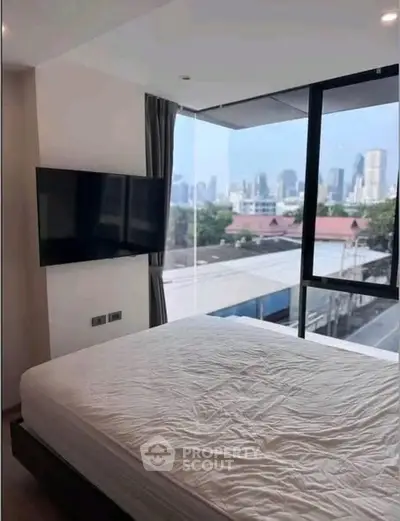 Modern bedroom with city view and wall-mounted TV in a high-rise apartment.