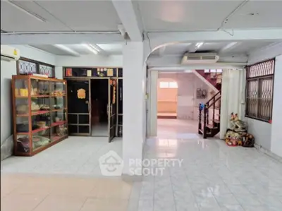 Spacious open-plan living area with tiled floors and ample natural light, featuring a display cabinet and staircase.