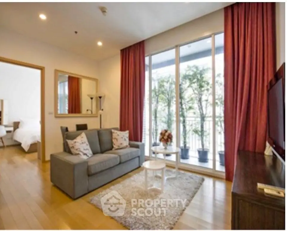 Spacious living room with cozy sofa and large windows opening to a balcony with greenery.