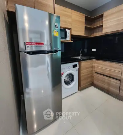 Modern kitchen with stainless steel fridge, washing machine, and wooden cabinets.