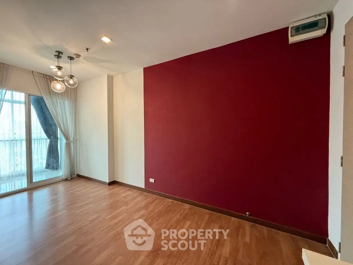 Spacious empty living room with red accent wall and large window view.