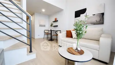 Modern living room with stylish decor and staircase, featuring cozy seating and elegant artwork.