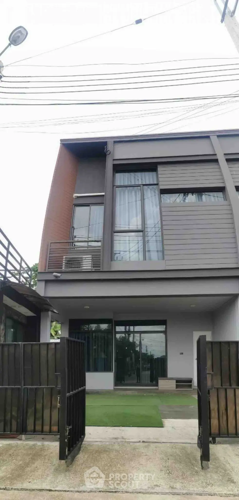 Modern two-story house with sleek design and gated entrance, featuring large windows and contemporary facade.