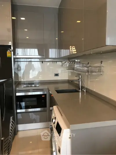 Modern kitchen with sleek cabinetry and built-in appliances, featuring a washing machine and oven.