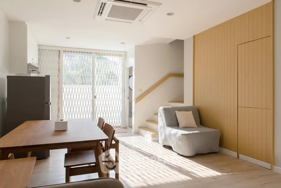 Bright modern living room with dining area and staircase, featuring natural light and minimalist design.