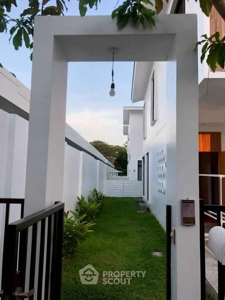 Modern white exterior with lush green garden and open gate entryway.