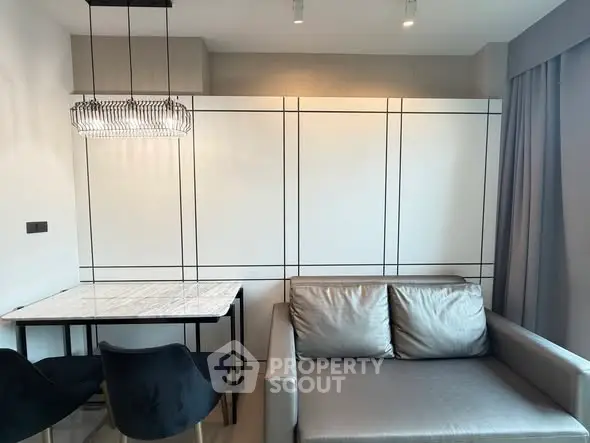 Modern living room with sleek sofa and elegant dining area featuring a chic chandelier.