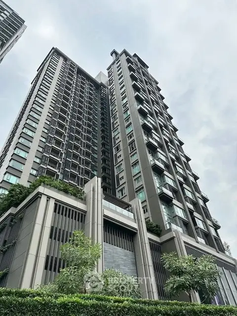 Modern high-rise condominium with sleek architecture and lush greenery in urban setting.