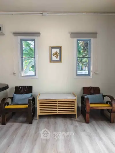 Charming living room with elegant wooden chairs and natural light from dual windows.